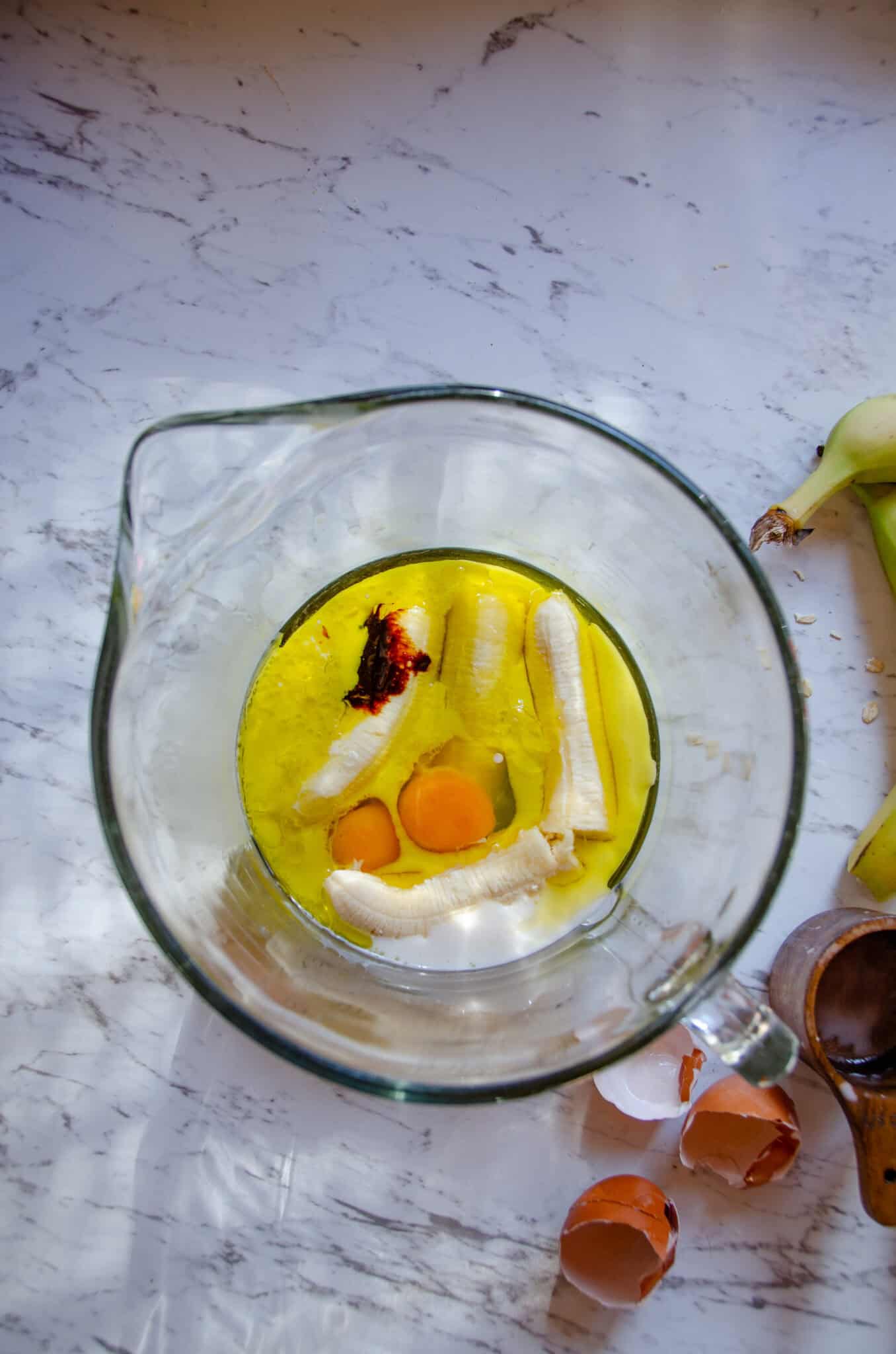 Eggs, olive oil, molasses, milk, banana in a glass mixing bowl.