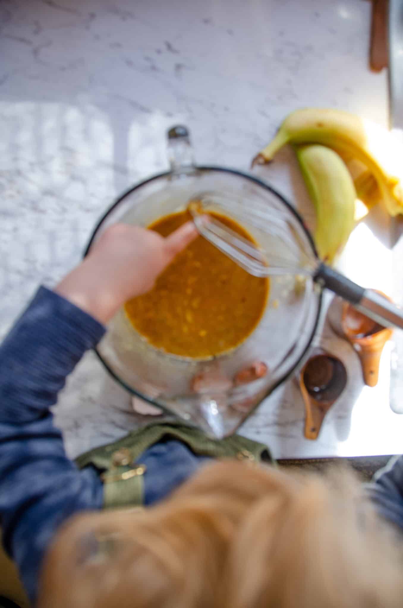 A child with a whisk mixing the protein bar batter together.