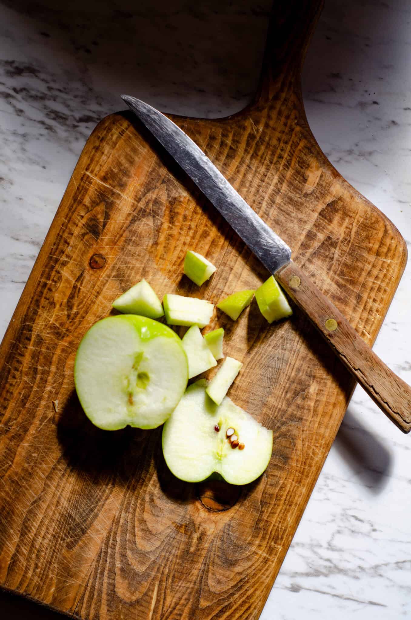 Chopping a green apple on a wood cutting board with a wood handle knife.