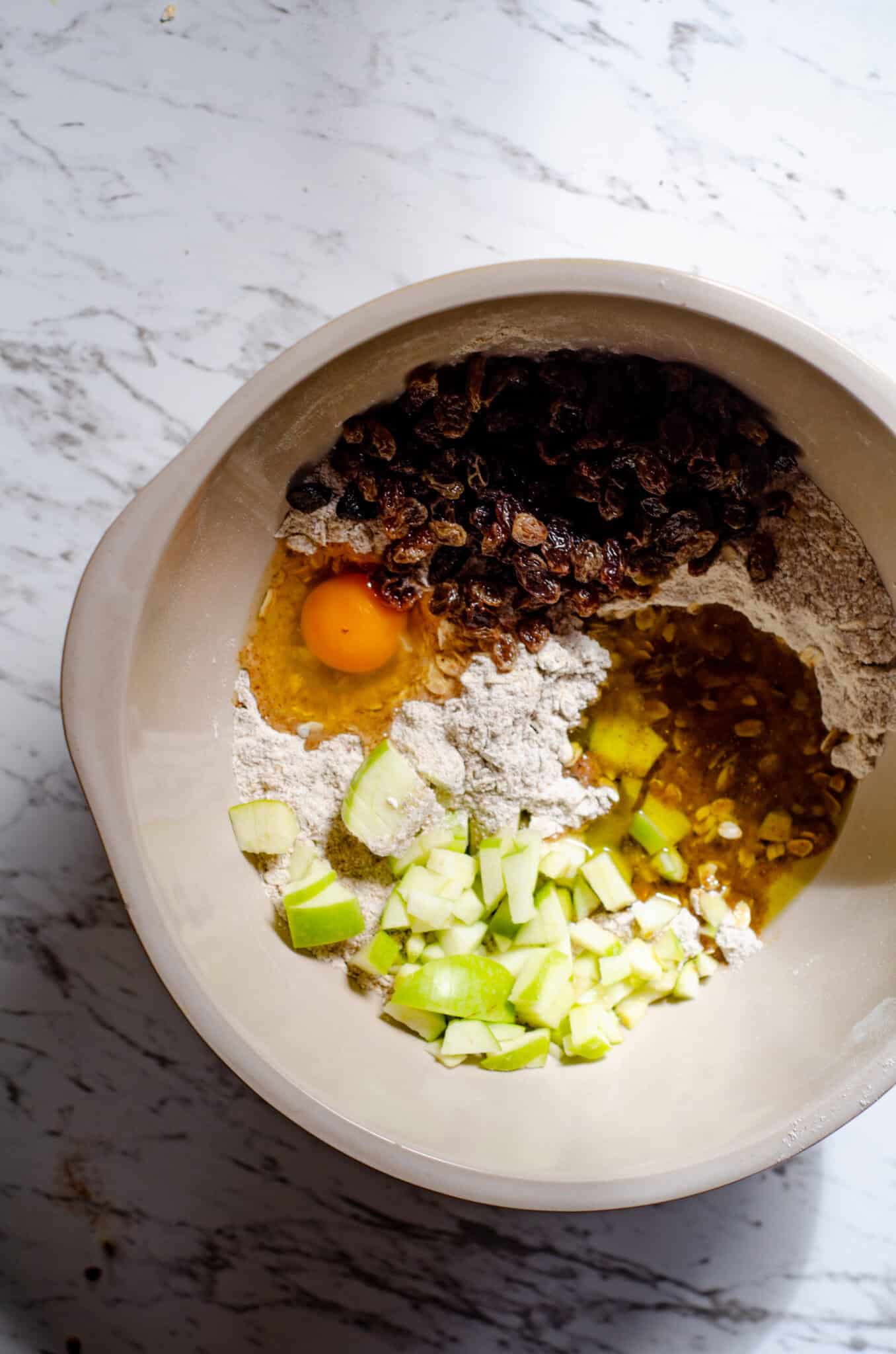 Egg, olive oil, and apple added to a bowl of dry ingredients for apple cookies.