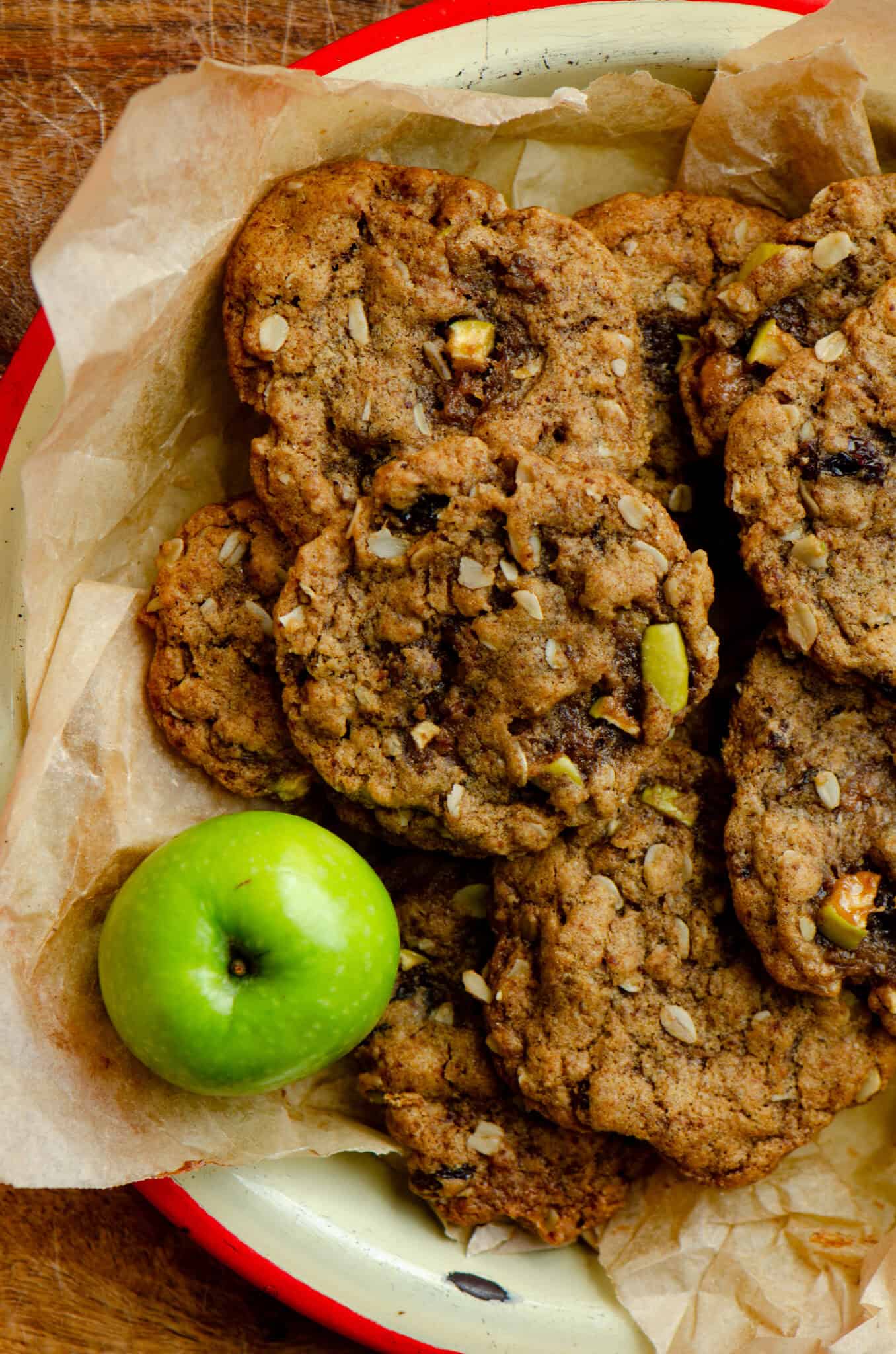 Light brown oatmeal apple cookies on a parchment paper on a plate with an apple beside it.