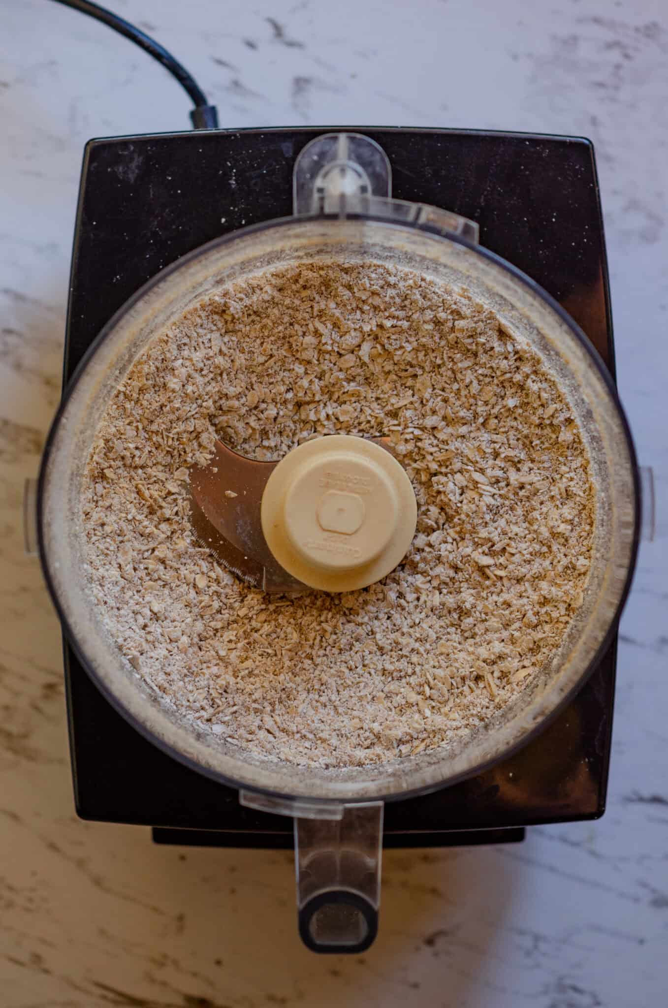 Rolled oats in a food processor that have been ground into a coarse powder.