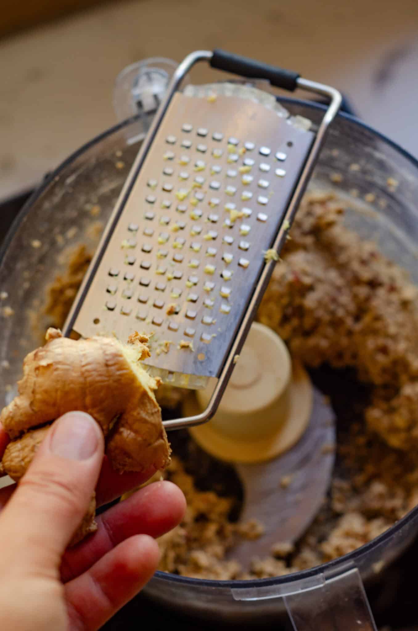 A small grater for ginger on top of the food processor with apple energy ball dough in it.