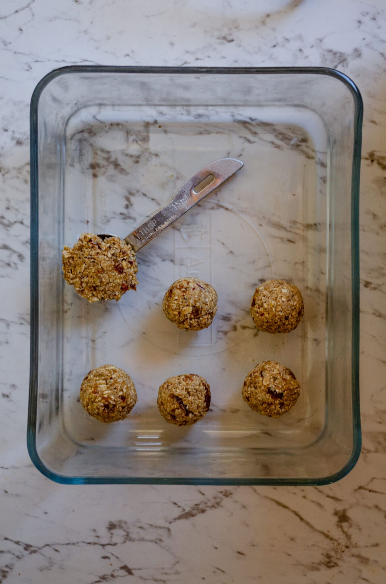 Rolling apple dough into energy balls with a tablespoon measuring spoon in a glass container.