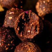 A bite out of a chocolate energy balls with specs of ground oatmeal and a flecks of dried rose.