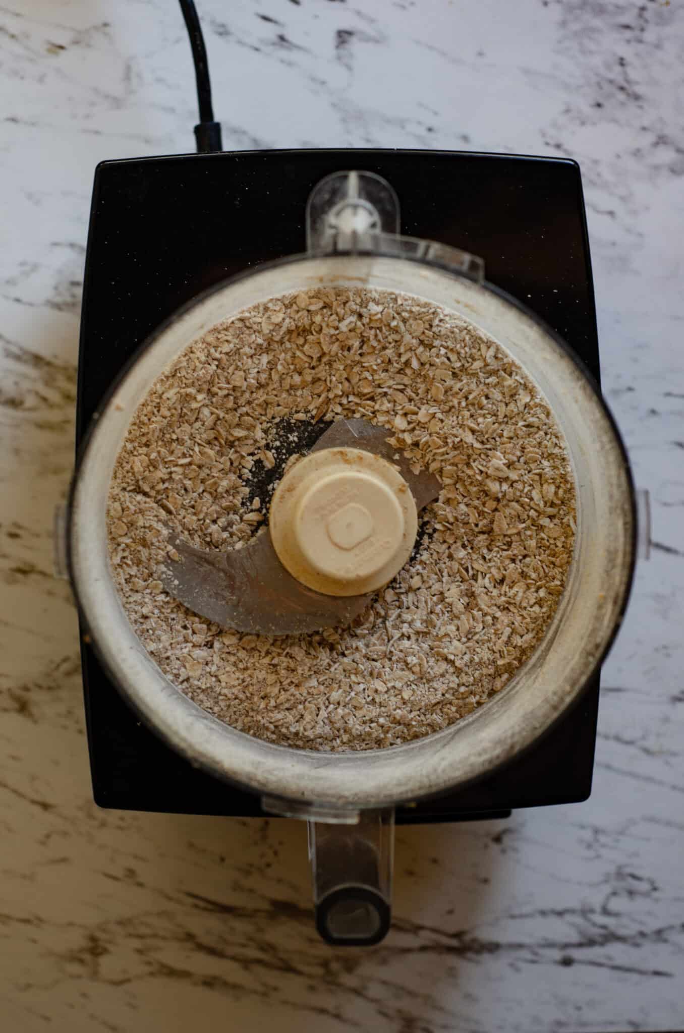 Rolled oats in a food processor that have been ground into a coarse powder.