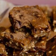 A brown moist bar with pieces of oats and chocolate chips visible stacked on two other bars with a bite out of the top protein bar.