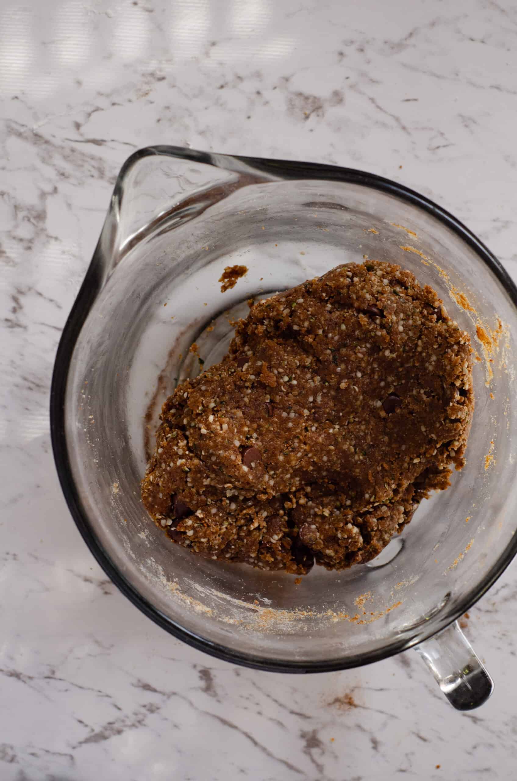 A ball of dark brown cookie dough in a glass mixing bowl.