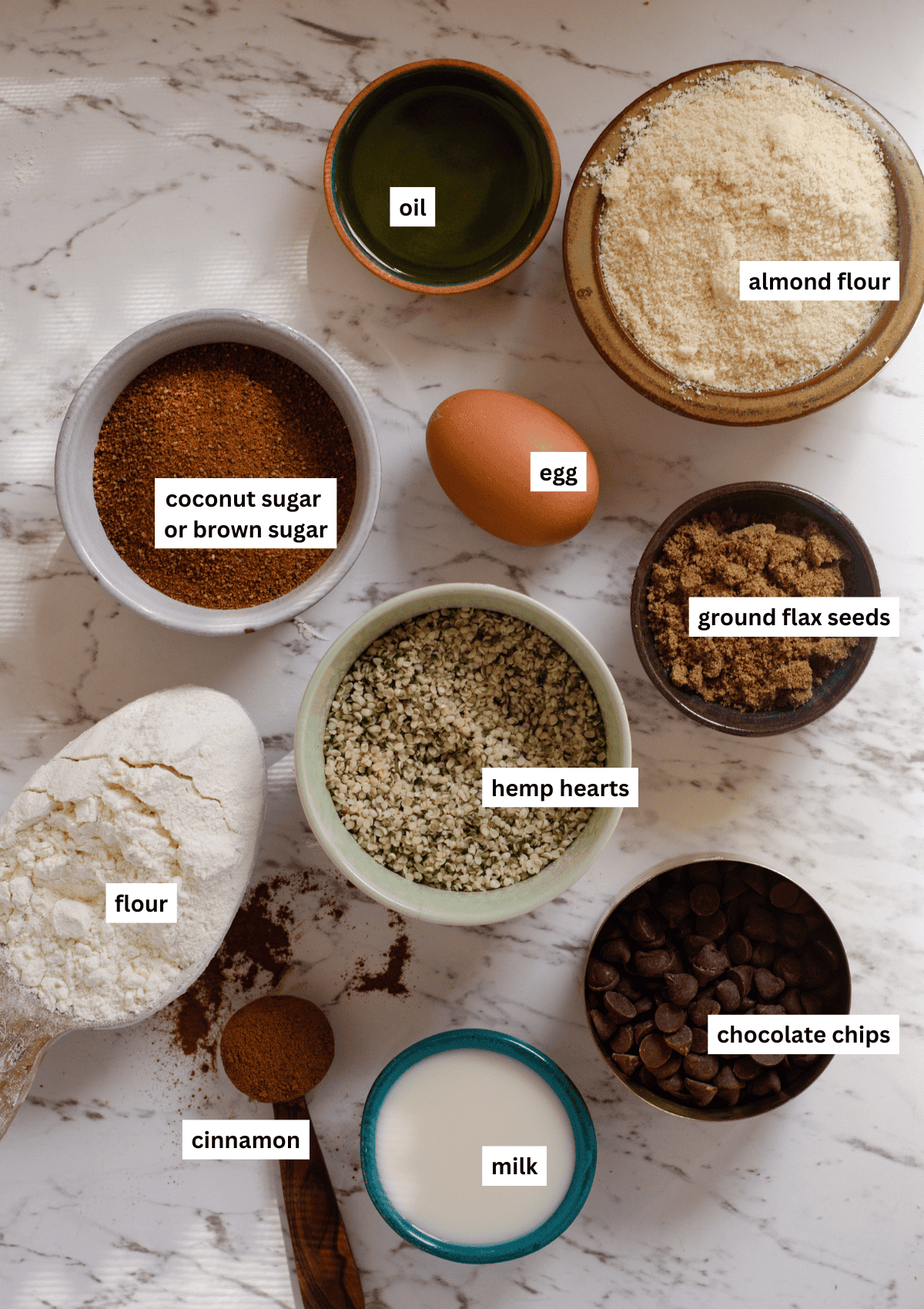 Ingredients for hemp cookies, including oil, almond flour, egg, coconut sugar, hemp hearts, flax seeds, milk, cinnamon, flour, and chocolate chips. 