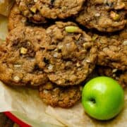 Light brown oatmeal apple cookies on a parchment paper on a plate with an apple beside it.