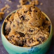 A scoop of cookie dough light brown with flecks of chocolate chips in it, in a light blue pottery bowl.