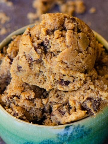 A scoop of cookie dough light brown with flecks of chocolate chips in it, in a light blue pottery bowl.