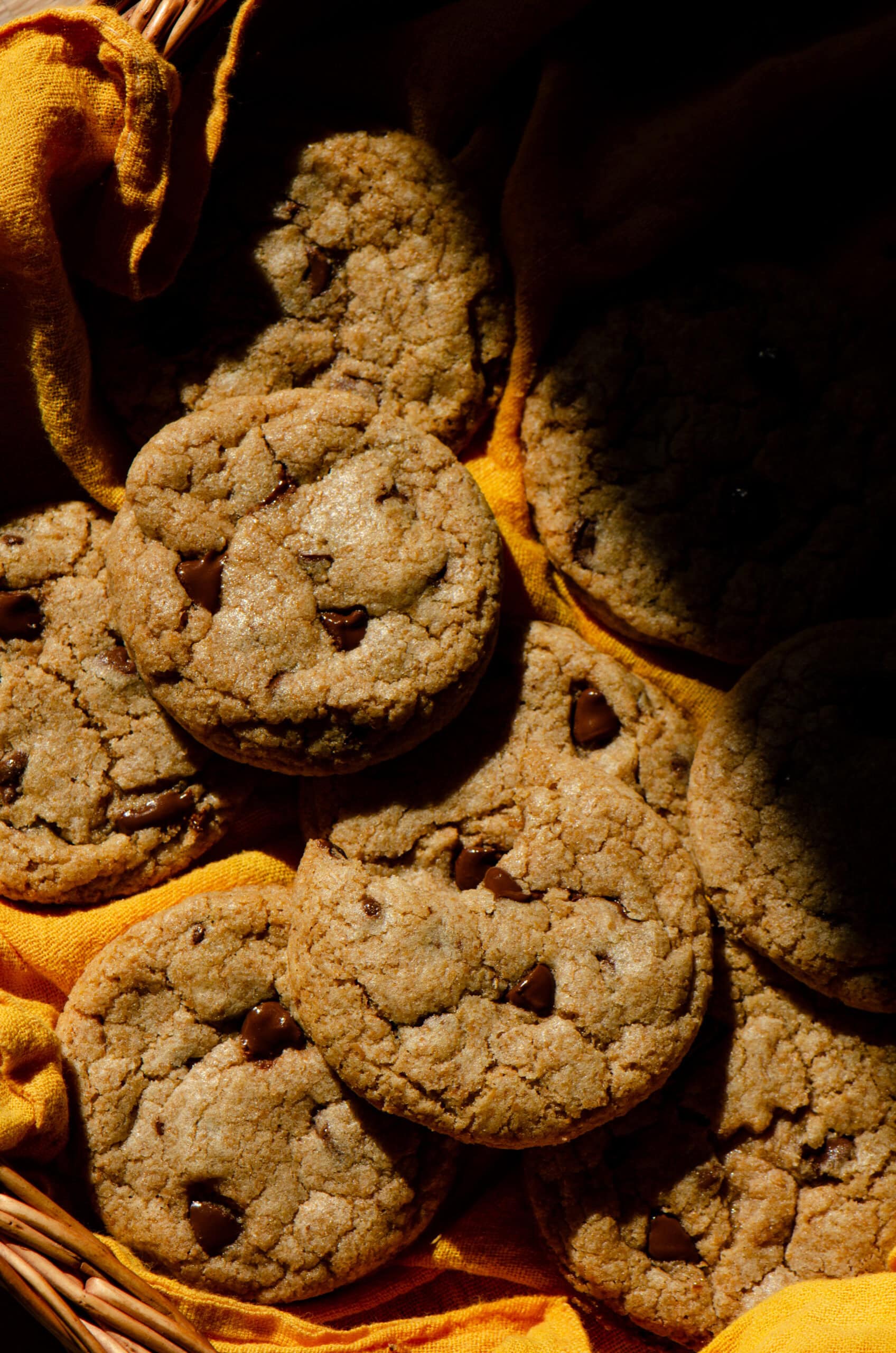 Whole wheat chocolate chip cookies with melted chocolate chips laying on top of each other on a bright yellow tea background. 