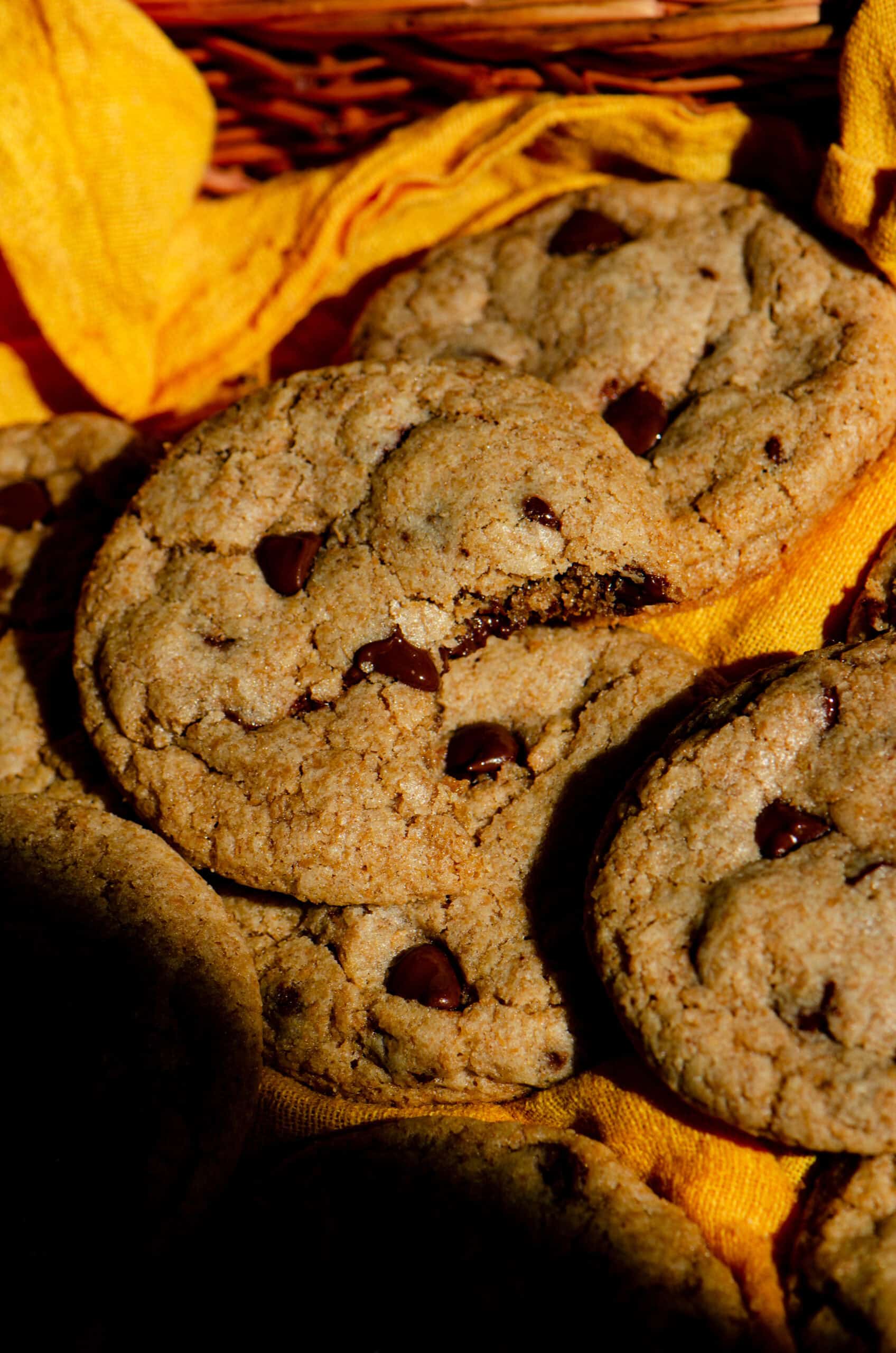 Thick chocolate chip cookie with melted chocolate chips warm from the oven with one bite missing on a yellow background.