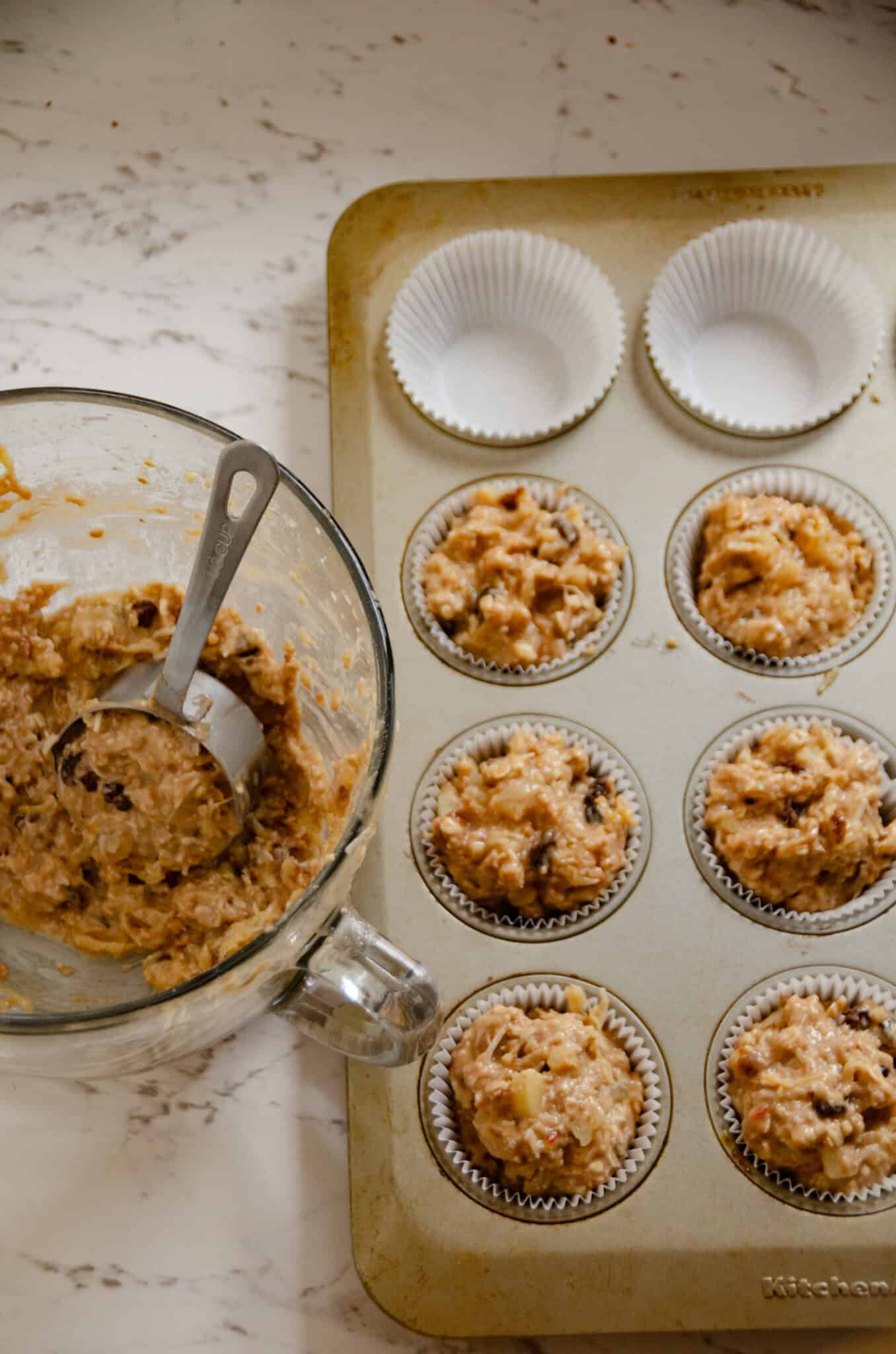Light brown muffin batter being scooped into the muffin pan with paper muffin liners.