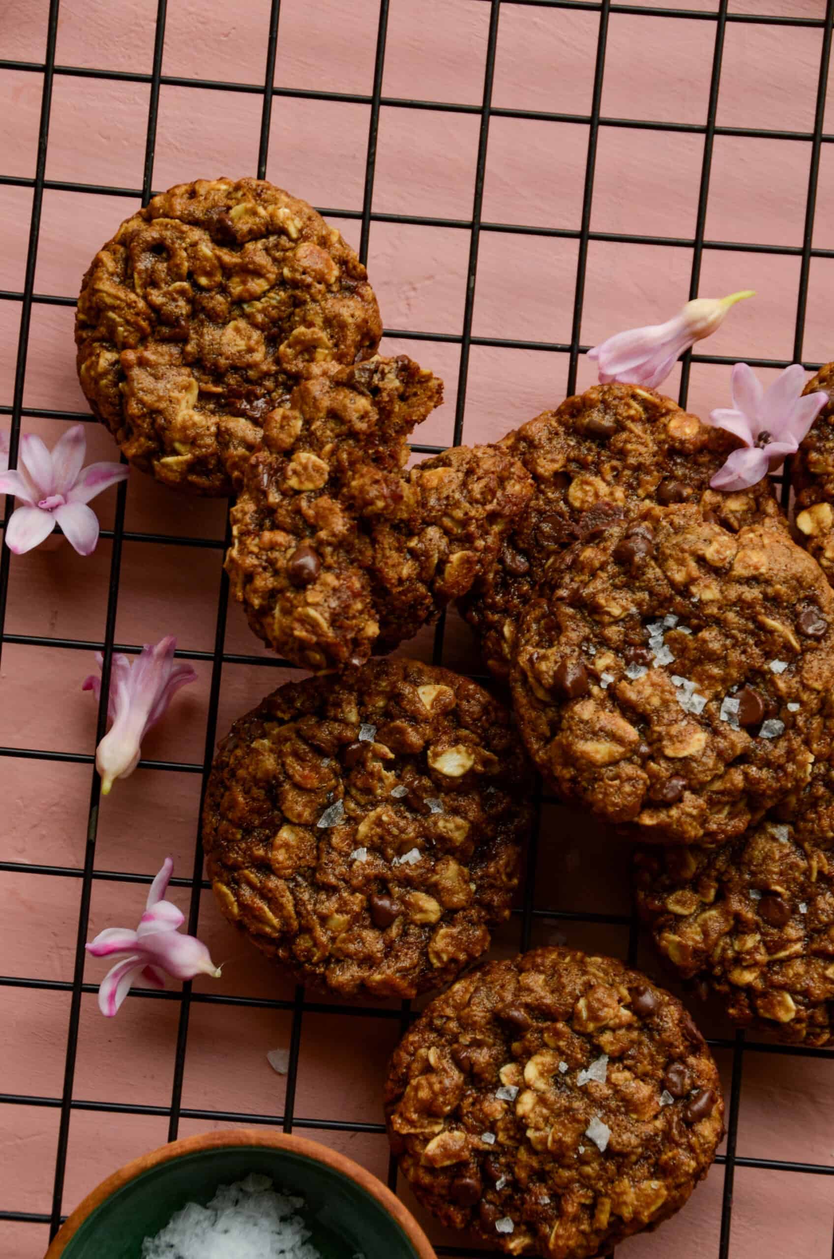 Banana oatmeal chocolate chip cookies cooling on a rack with pink flowers and some sea salt.