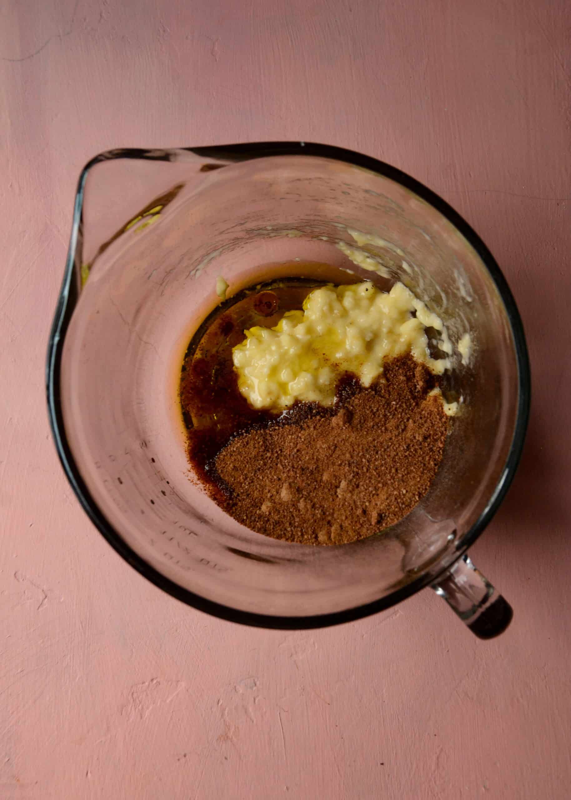 Mashed banana, coconut sugar, olive oil, and vanilla in a glass mixing bowl.