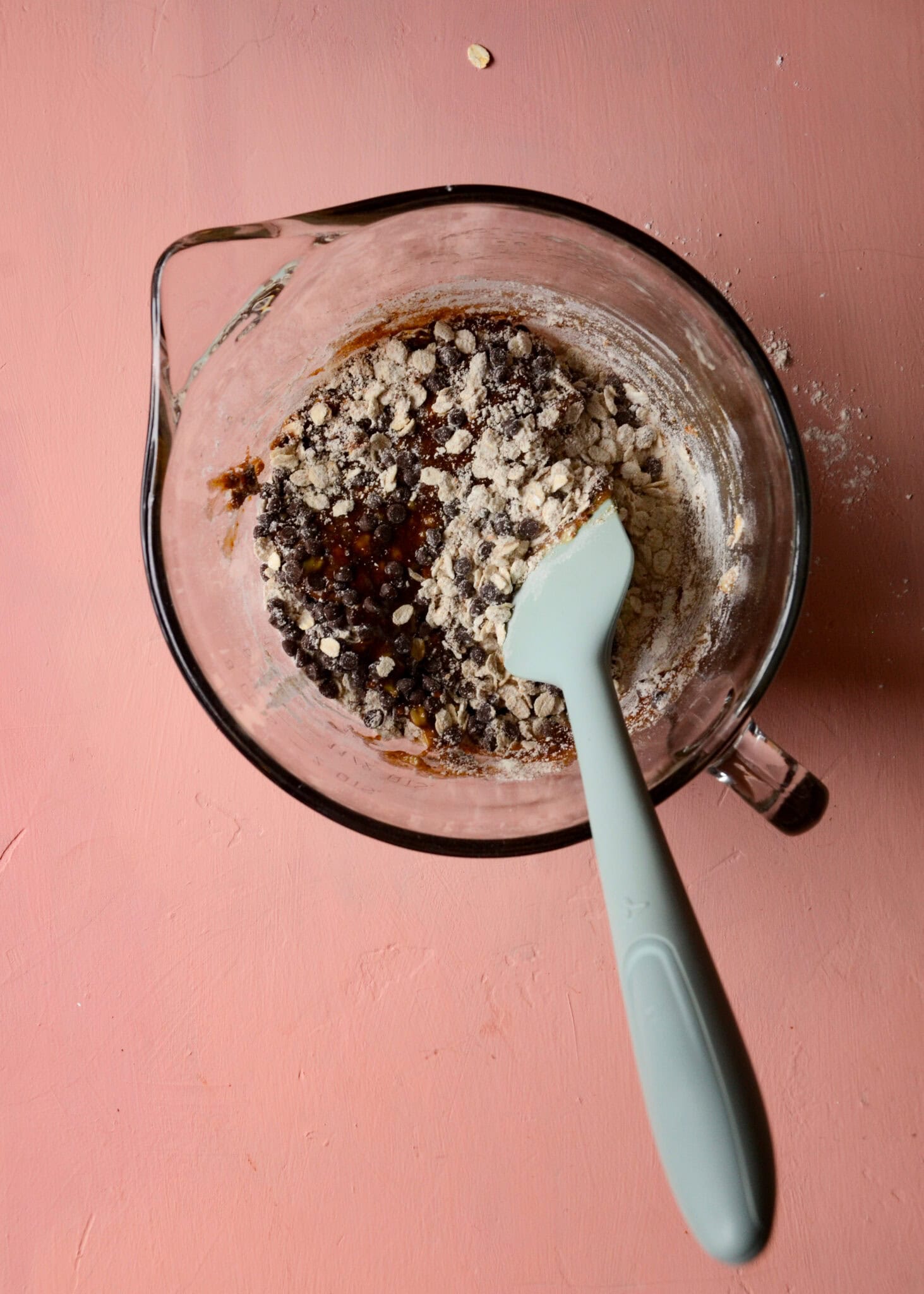 Dry ingredients being mixed into the wet cookie ingredients in a glass mixing bowl with a blue spatula.