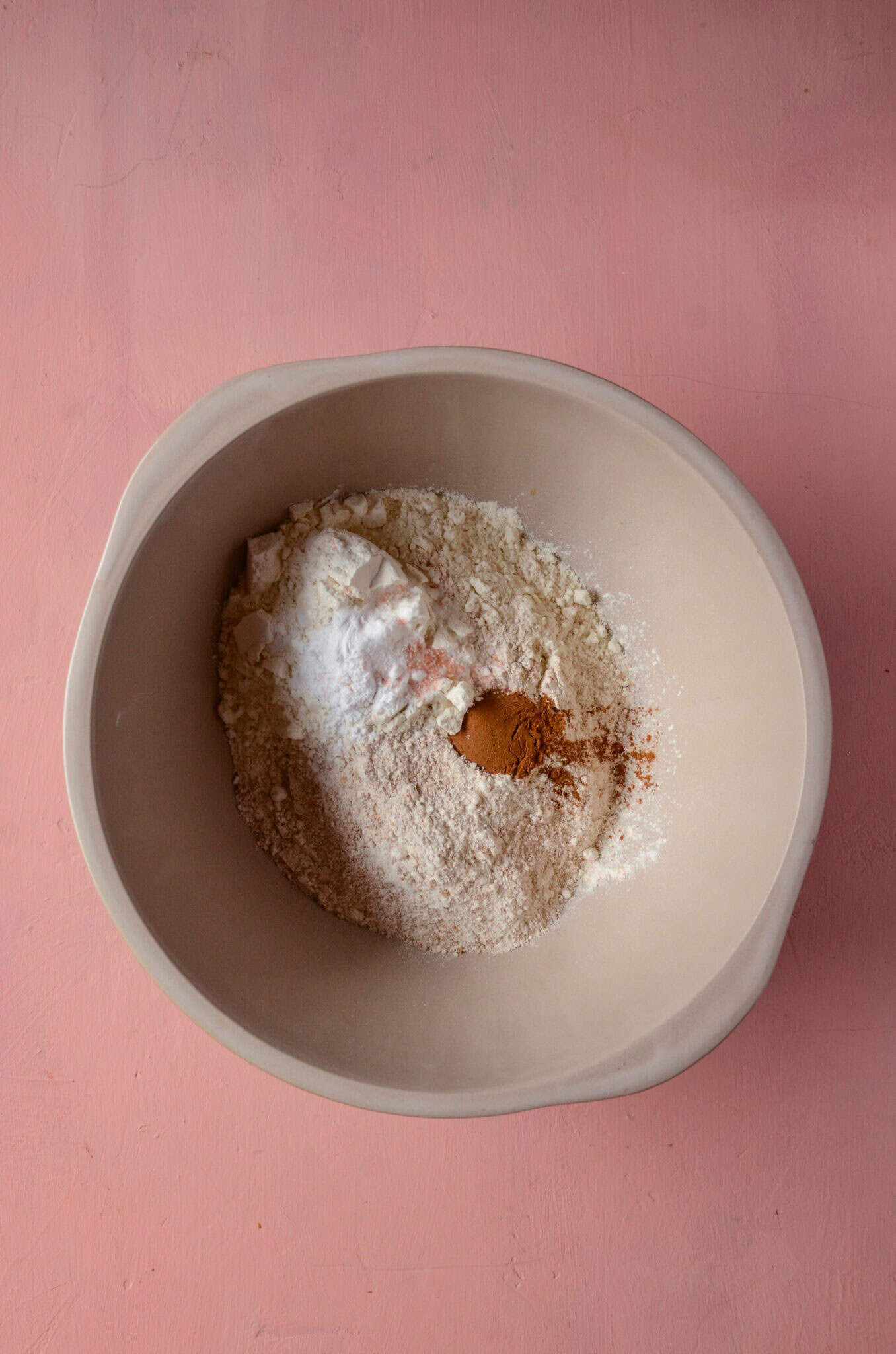 A mixing bowl with flour, baking soda, baking powder, salt, and cinnamon.
