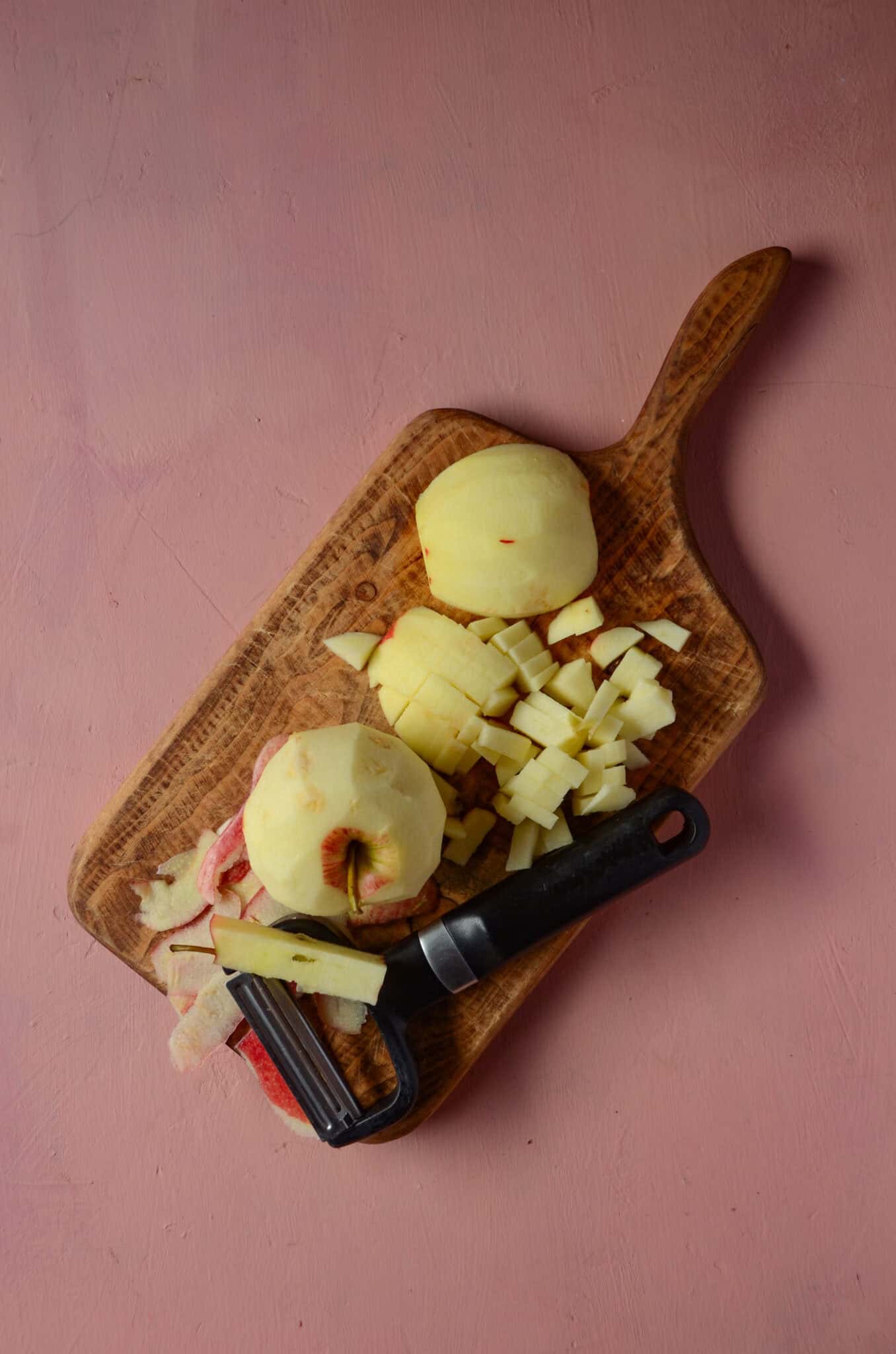 Two apples, an apple peeler and chopped apples on a wooden cutting board.