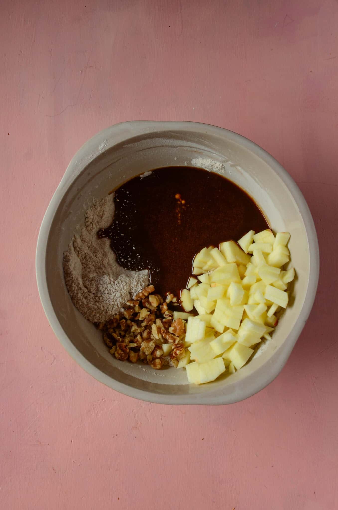In a large mixing bowl there is flour, egg mixture, chopped apples and walnuts for snack cake.