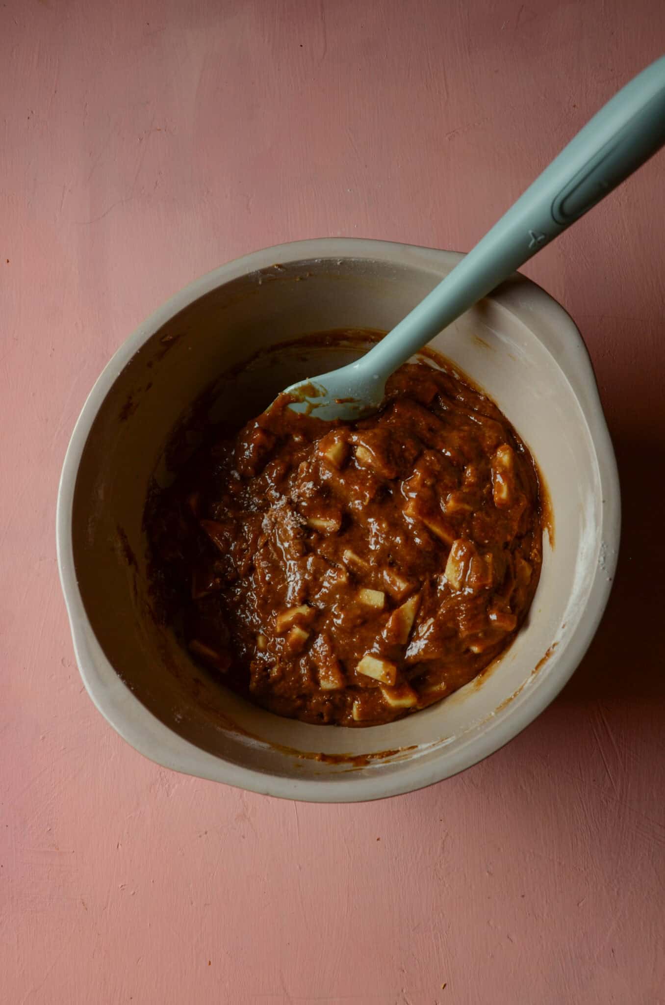 Brown apple cake batter in a mixing bowl with a spatula folding the batter together.