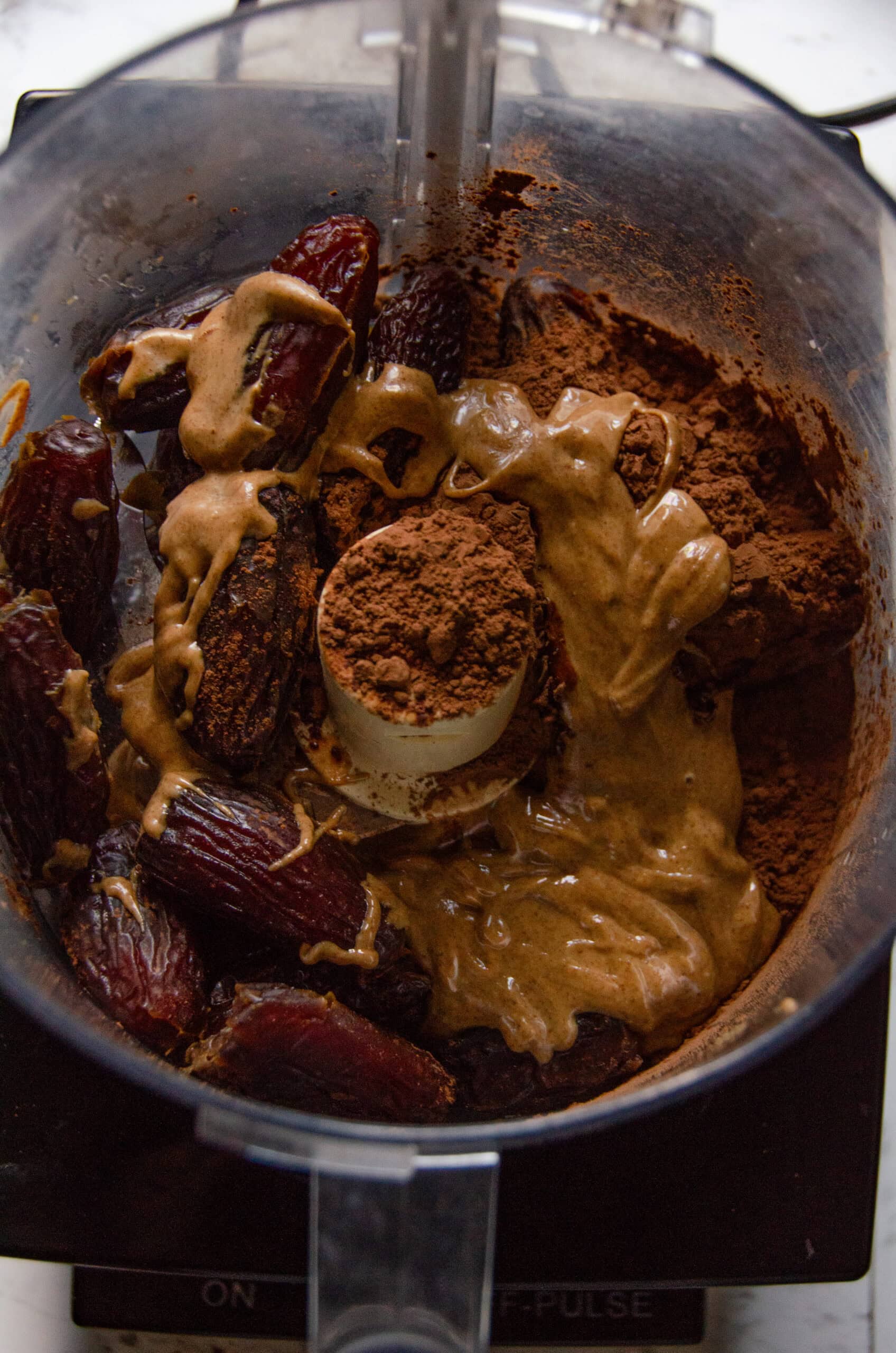 A food processor with almond butter, dates, and cocoa powder about to be blended in it.