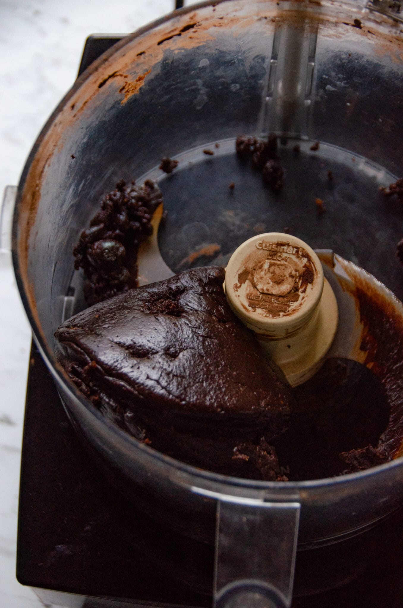 A shiny ball of chocolate date brownie batter in a food processor.