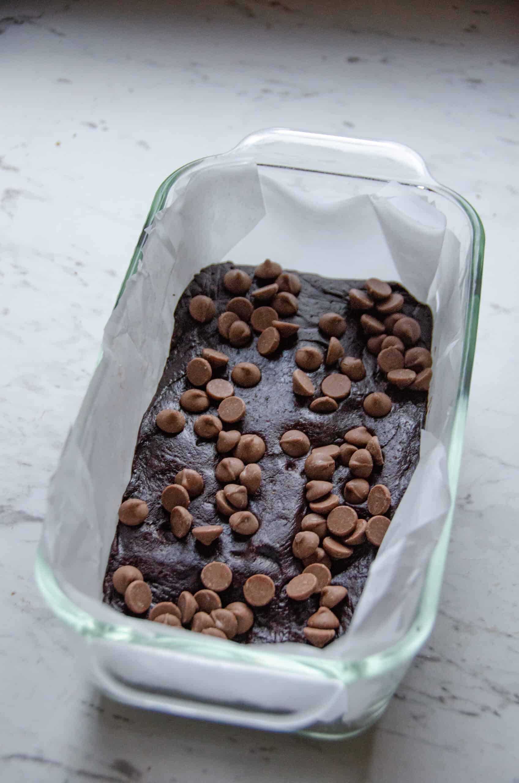 Thick brownie batter made with dates pressed into a loaf pan with chocolate chips on top.