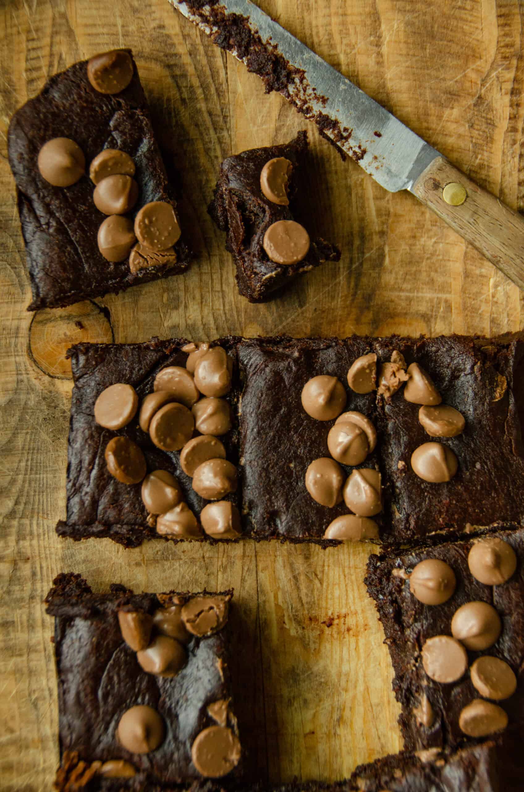 Slices of brownie with chocolate chips on a wood cutting board with a knife that has crumbs on it.