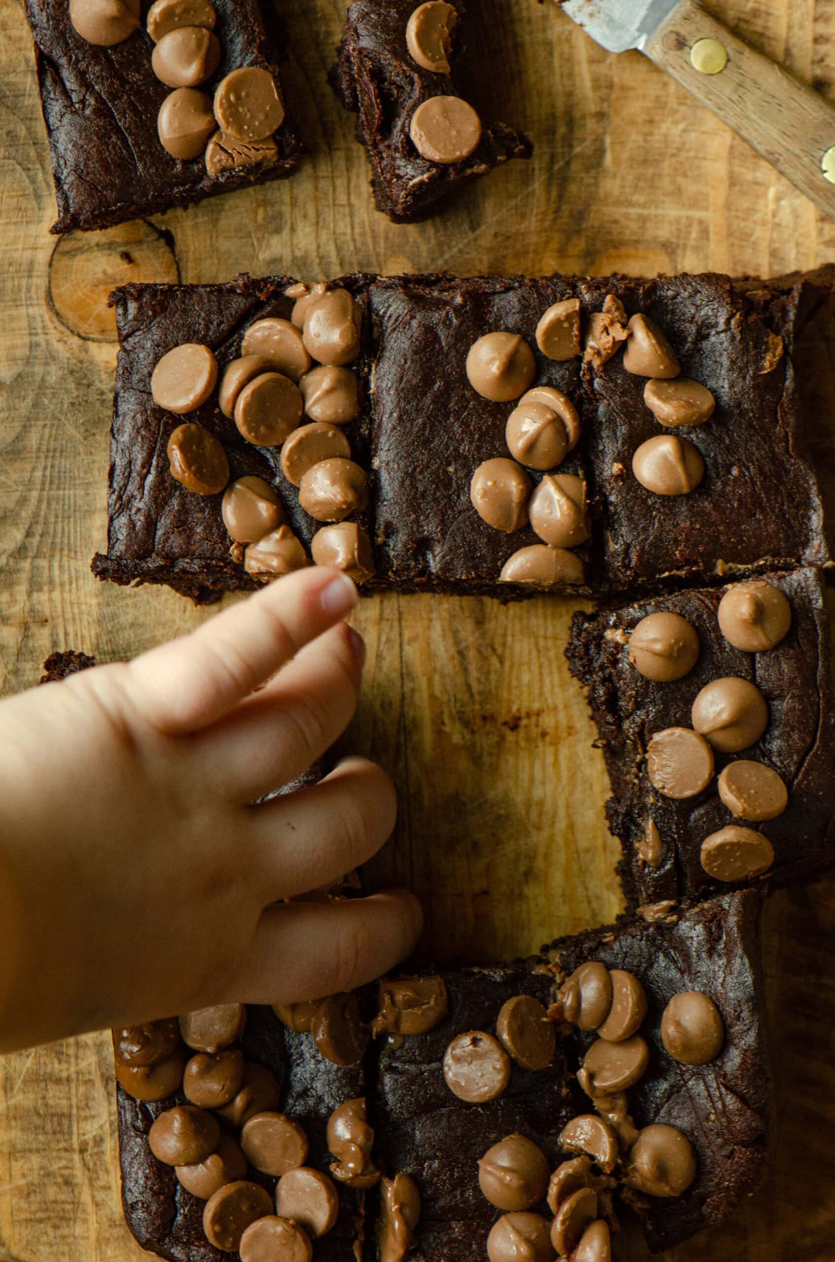 A toddler hand reaching to grab a slice of healthy brownies made with dates.