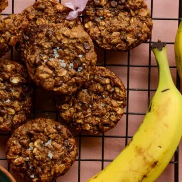 A banana on a cooling rack with vegan oatmeal chocolate chip cookies.