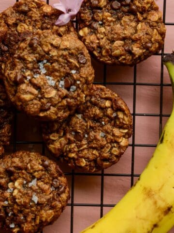 A banana on a cooling rack with vegan oatmeal chocolate chip cookies.