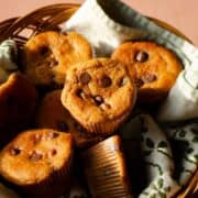 A basket with a tea towel with muffins that have chocolate chips on top/