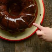 Toddler poking a finger at a brown glazed apple bundt cake.