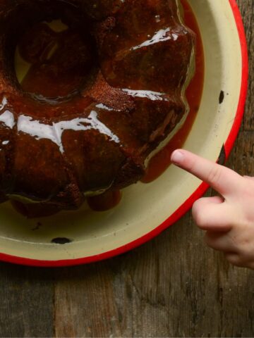 Toddler poking a finger at a brown glazed apple bundt cake.