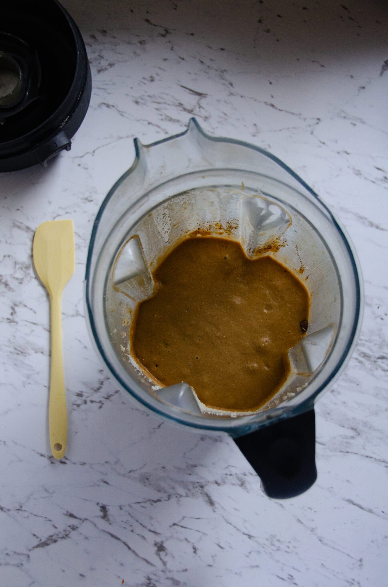 A vitamix with chocolate chip muffin batter and a spatula beside it.