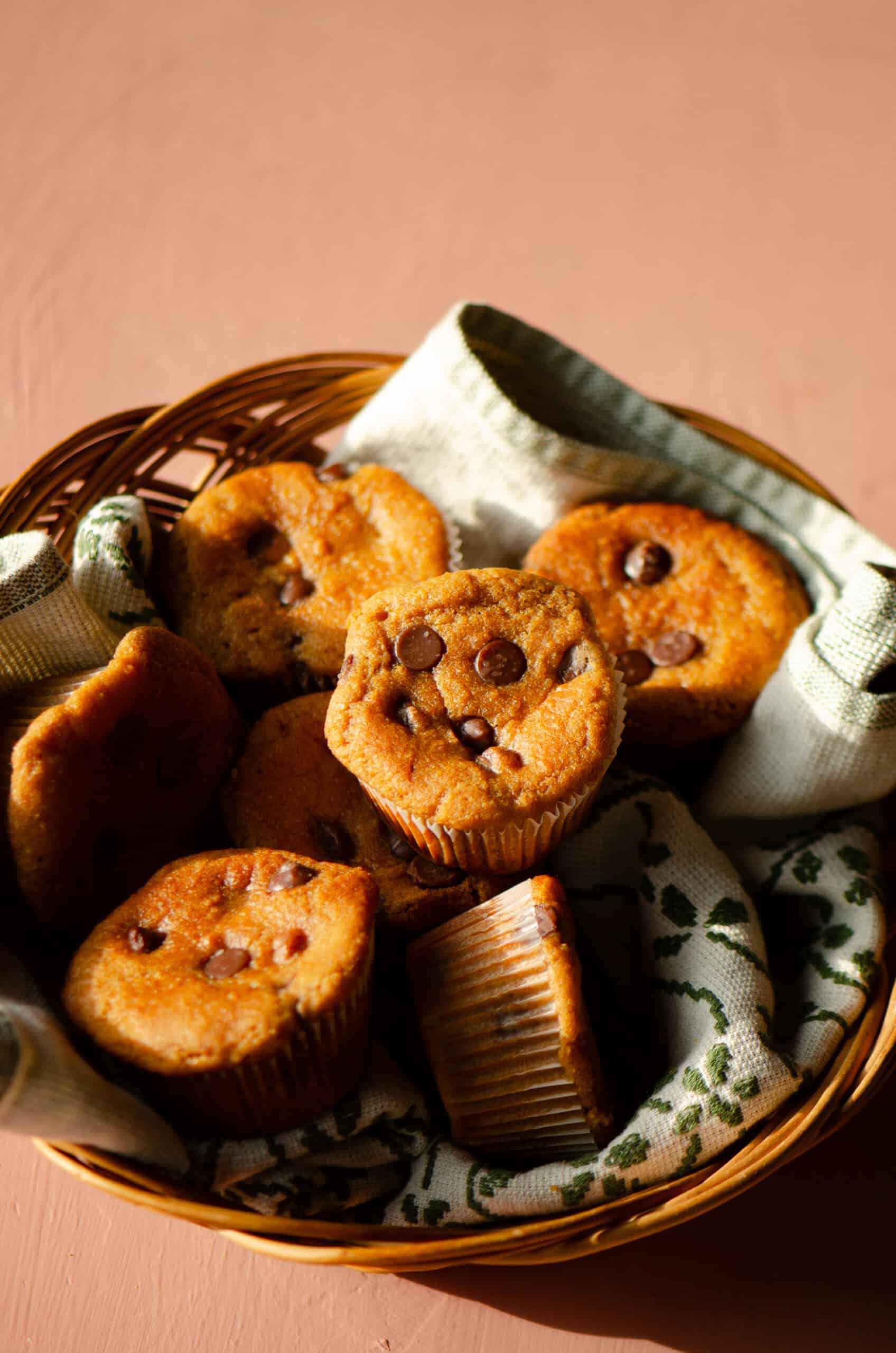 A basket with a tea towel with muffins that have chocolate chips on top/