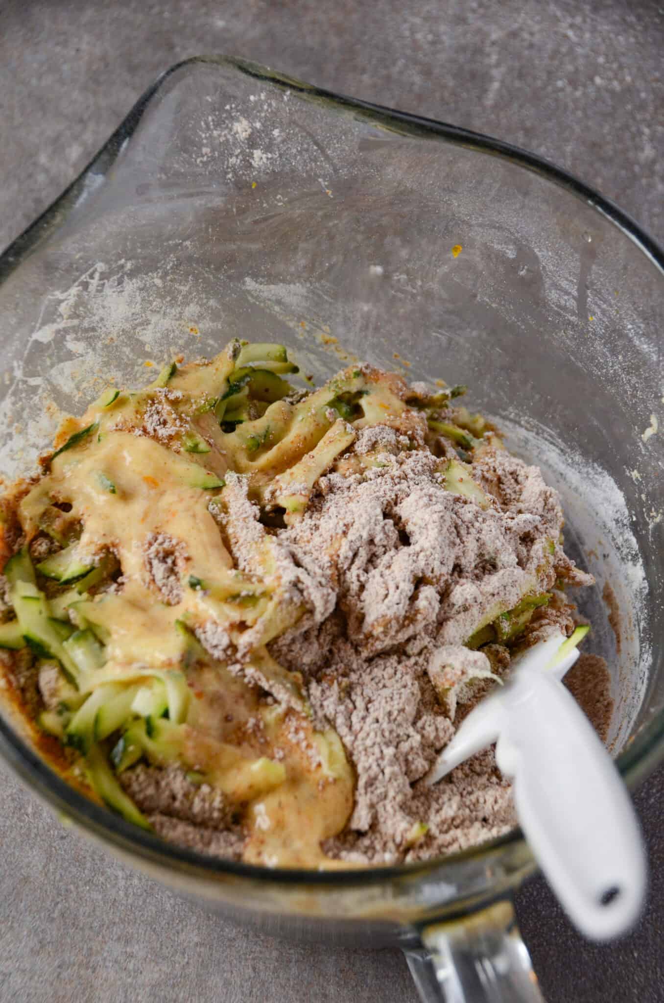 Folding together muffin batter in a glass mixing bowl with a spatula.