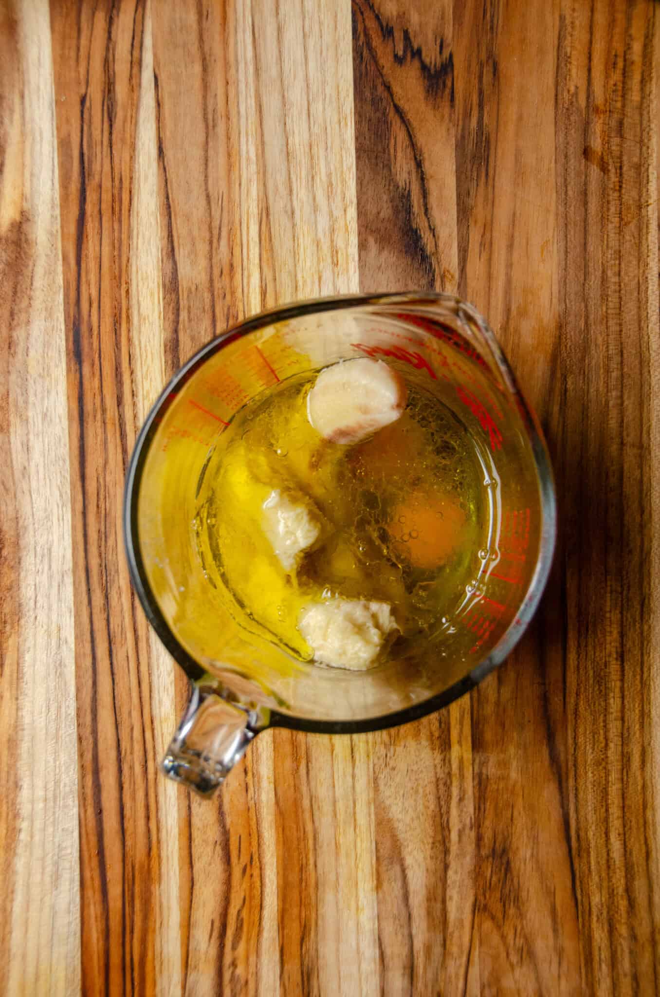 A large glass measuring cup with bananas, eggs, oil.