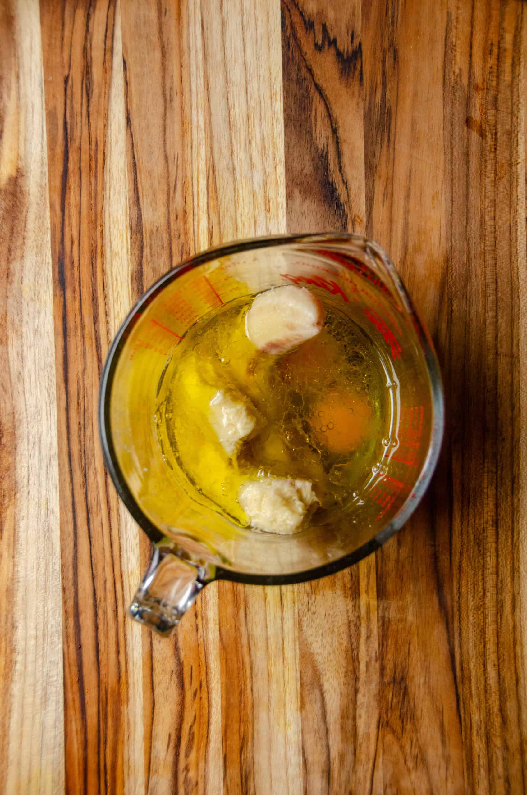 A large glass measuring cup with bananas, eggs, oil.