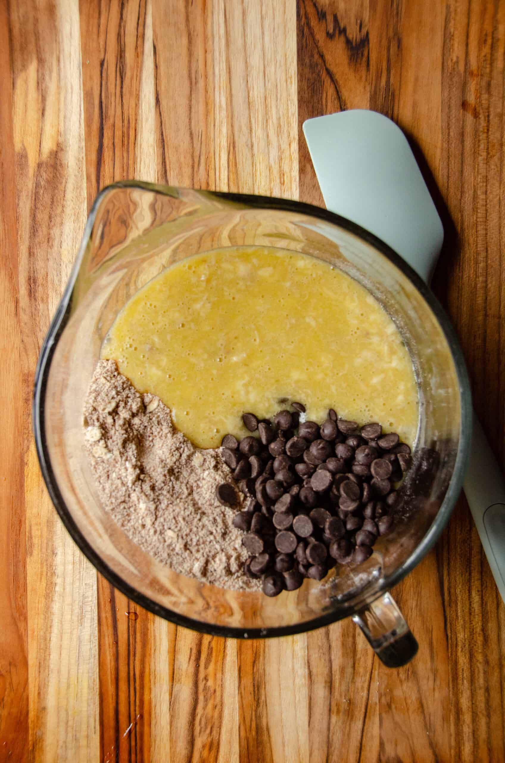 Ingredients for muffins in a bowl with chocolate chips and a spatula on the counter.