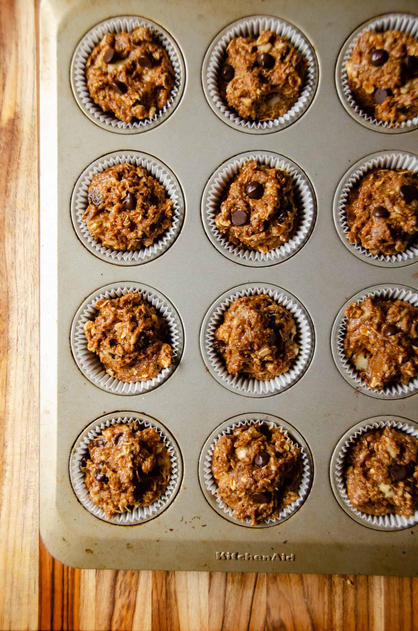 Banana chocolate chip muffin batter in paper muffin liners in a muffin pan.