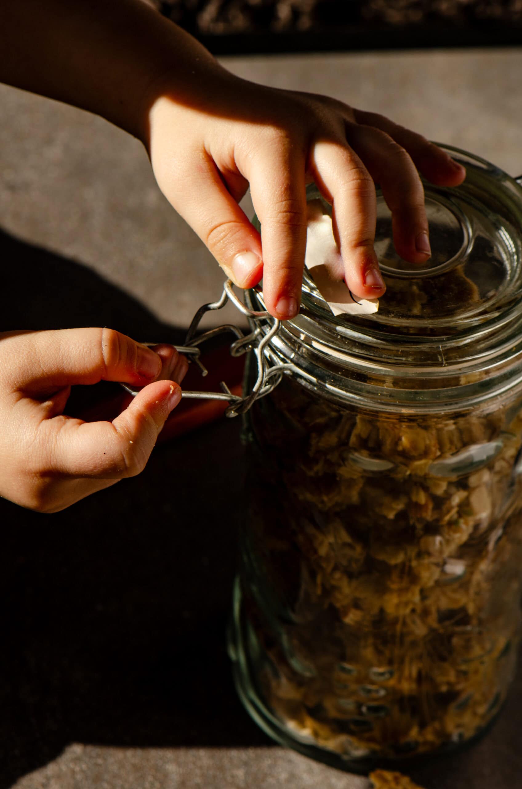 A child opening a metal clasp on a jar of granola.