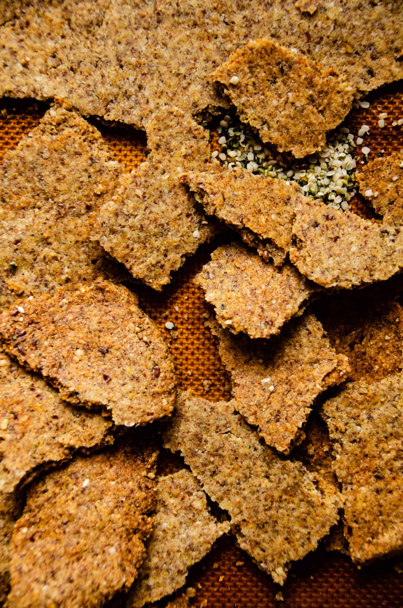 Broken homemade cracker pieces on a baking sheet with hemp hearts under them.