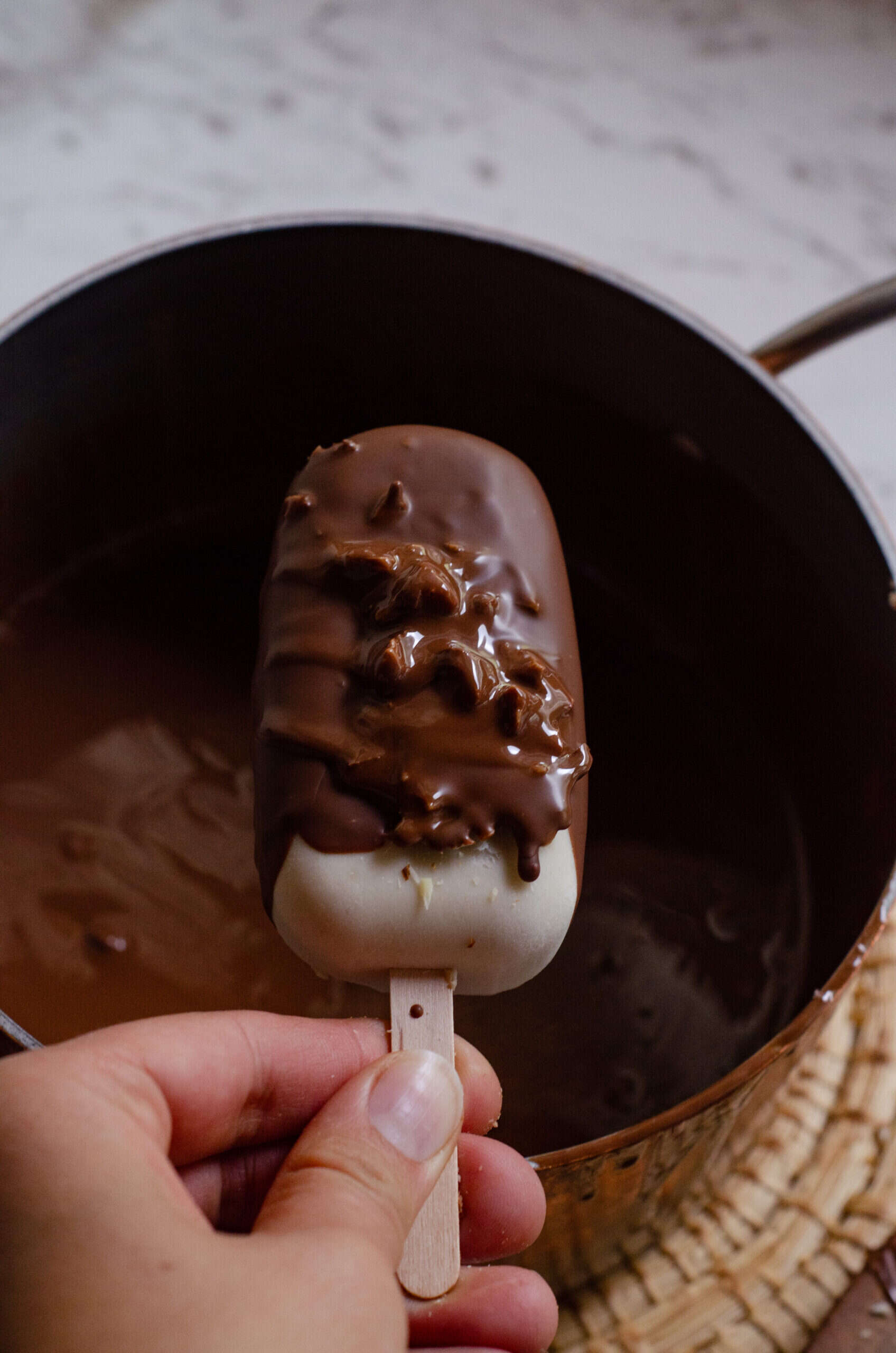 A ice cream bar being dipped into melted chocolate chips.