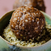 A brown energy balls sitting in a small bowl filled with hemp hearts.