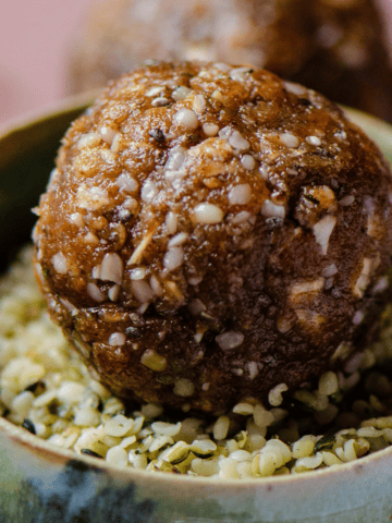 A brown energy balls sitting in a small bowl filled with hemp hearts.