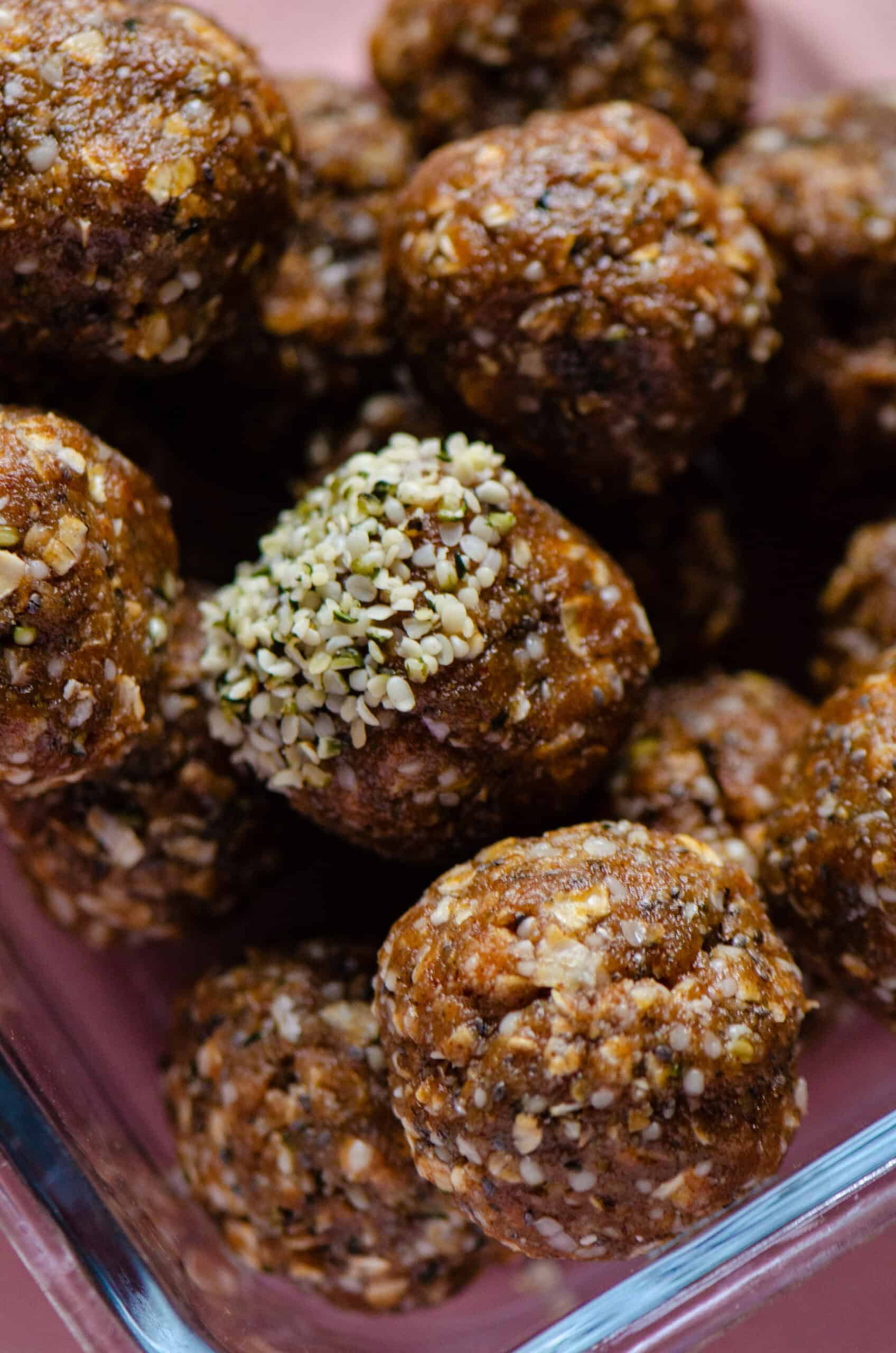 A stack of brown energy balls with seeds in them and the one in the middle half covered in hemp hearts.