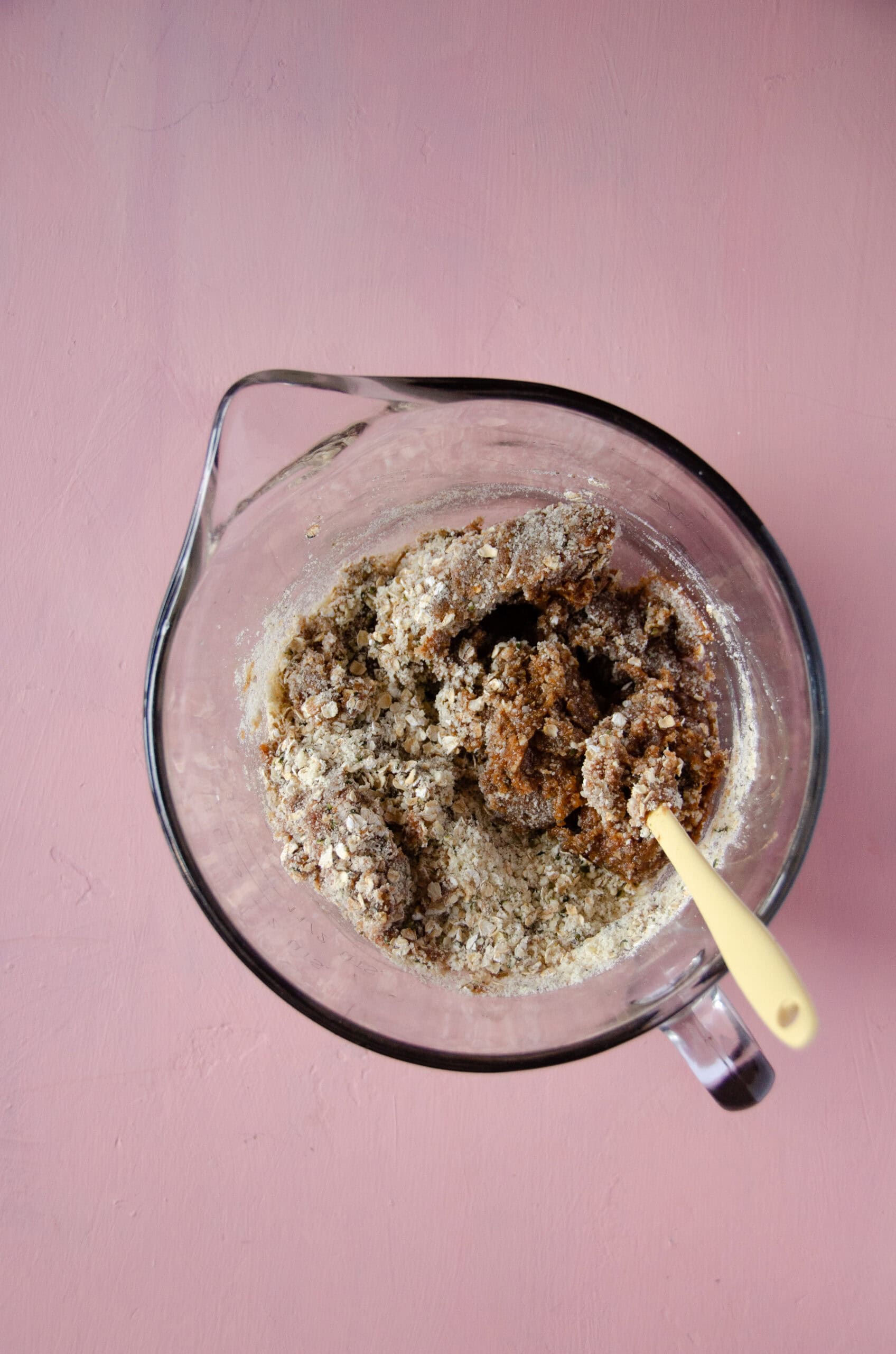 A glass mixing bowl with a little yellow spatula stirring dough for protein bites.